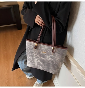 Dettaglio della borsa tote grigia marmorizzata con manici marroni e logo dorato