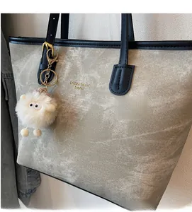 Detail of grey-green tote bag with black leather straps and a fuzzy monster charm