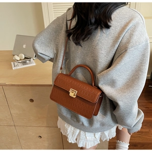Detailed view of a brown crocodile pattern shoulder bag with a gold metal clasp buckle