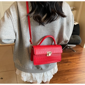 Detail of red crocodile textured handbag with golden twist lock worn by a model