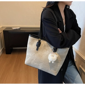 Detail of gray tote bag texture with black strap, gold hardware and plush sheep charm