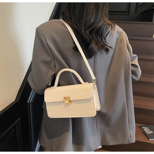 Detail of cream white croc-effect leather handbag with gold metal clasp on a grey suit model
