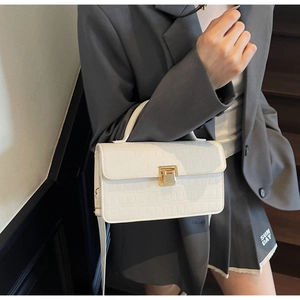 Detail of white crocodile pattern shoulder bag with gold clasp worn by a fashion model