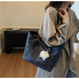 Detail of grey washed texture tote bag with gold logo and plush charm accessory