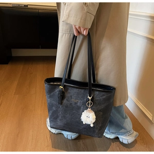 Detail of dark grey contrast tote bag with black handles and white plush charm accessory
