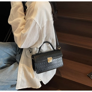 Detail of black crocodile pattern faux leather handbag with elegant gold metal lock clasp