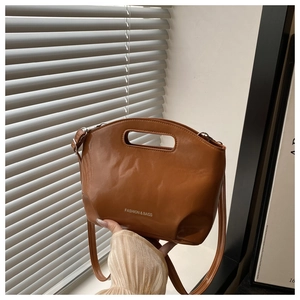 Detail of a brown leather crossbody bag with cutout handle and white fashion text branding