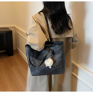 Detail of dark gray tote bag with Fashion text and white plush charm on model
