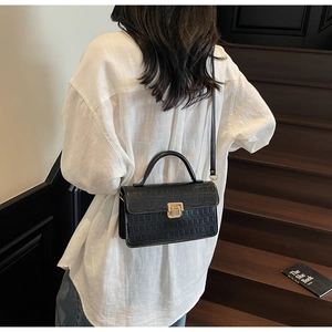 Detail of black crocodile texture bag with gold lock shown in a lifestyle street setting