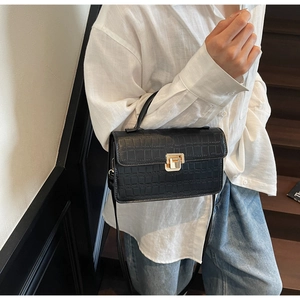 Detail of black crocodile texture bag featuring gold clasp and top handle in lifestyle setting