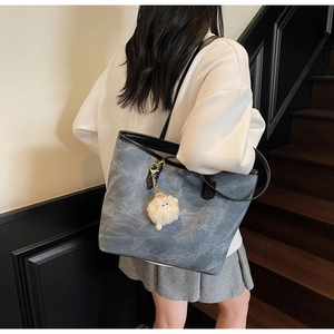 Detail of navy denim tote bag with black leather straps and cute sheep plush charm