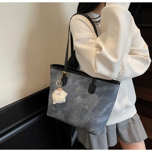 Detail of grey-blue tote bag with marble texture, gold lettering and plush charm
