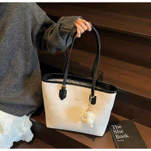 Detail of a black and white contrast tote bag with a plush charm on a wooden background