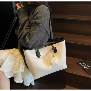Detail of cream tote bag with black trim and fluffy monster charm on wooden stairs