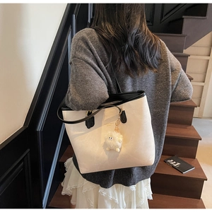 Detail of contrast tote bag with plush charm on a wooden staircase setting