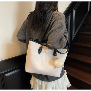 Detail of cream contrast tote bag with black straps and plush ball charm on shoulder