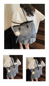 Detail of grey marble textured tote bag with black leather handle and plush pompom charm