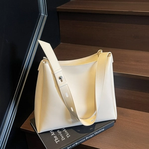 Minimalist cream leather tote bag with wide shoulder strap on dark wooden stairs