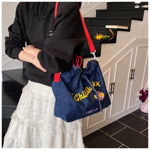 Detail der blauen Denim-Tasche mit rotem Schultergurt und gelber Stickerei-Applikation