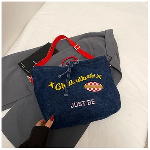 Detail der blauen Denim-Tasche mit rotem Gurt und Stickerei auf einem grauen Jackett