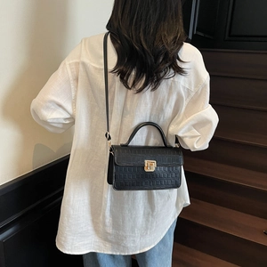 Chic black crocodile pattern handbag with gold clasp on white shirt and jeans model