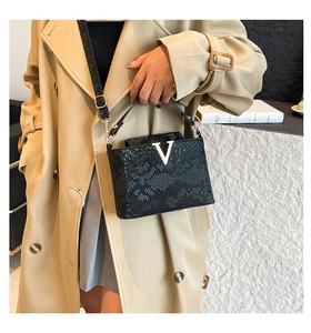 Detail of black crocodile texture handbag with silver V-buckle and adjustable strap