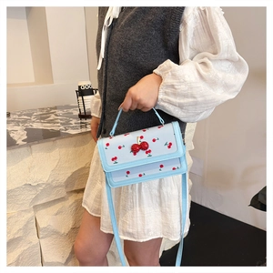 Dettaglio della borsa a tracolla azzurra con stampe di ciliegie e fibbia a ciliegia brillante
