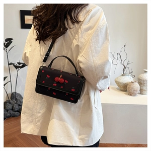 Dettaglio del ricamo di ciliegie rosse e ciondolo di strass su borsa a tracolla in pelle nera