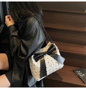 Sac bandoulière élégant noir et blanc avec nœud porté par un mannequin en extérieur