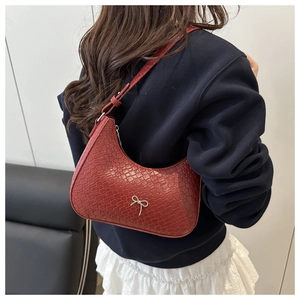 Detail of red crocodile pattern underarm bag with silver bow on a female model