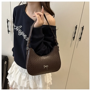 Detailed view of woven texture and silver bow on dark brown leather underarm bag