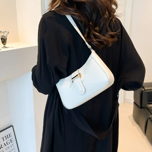 Minimalist off-white leather shoulder bag with a gold H-buckle worn by a model