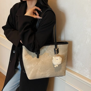 Minimalist sand-colored tote bag with black leather straps and plush lamb charm worn by a model