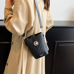 Chic black woven texture crossbody bucket bag with silver twist lock on khaki trench coat