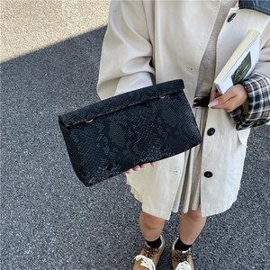 Minimalist black python pattern envelope clutch bag held at 45-degree angle outdoors