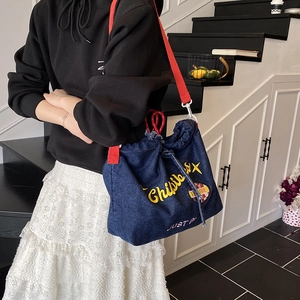 Blue denim drawstring crossbody bag with red strap and embroidery in street style