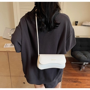 Détail d'un sac à bandoulière blanc minimaliste avec inscription dorée et fine bandoulière