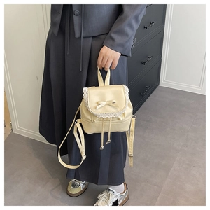 Detail of a beige ballet-core mini bag featuring lace trim and a bow on grey attire