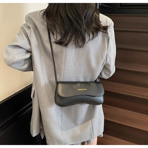 Détail du sac baguette noir avec base ondulée et lettrage doré sur un mannequin