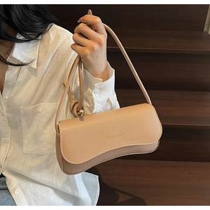 Détail d'un sac sous le bras beige montrant le logo FASHION & BAGS et le rabat incurvé chic