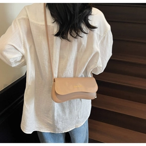 Détail d'un mannequin portant un sac bandoulière beige sur un escalier en bois