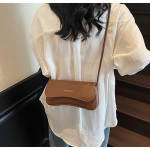 Détail du sac bandoulière marron caramel avec texte doré sur un rabat ondulé chic