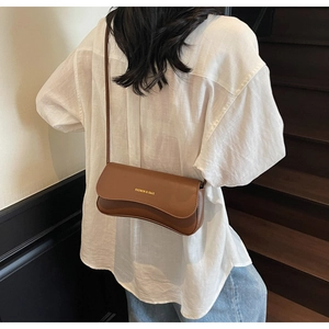 Détail du sac bandoulière en cuir marron caramel avec rabat ondulé sur mannequin en blanc