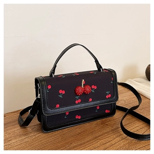 Close-up of black cherry print crossbody bag with 3D cherry decoration on wood table