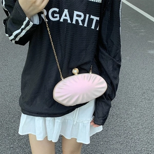 Chic pearl pink shell evening clutch bag with gold chain strap worn by a model