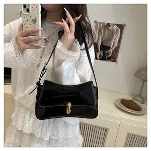 Detail view of a black patent leather shoulder bag with a gold oval metal clasp