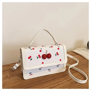 Detail of white mini crossbody bag featuring red cherry prints and a 3D cherry charm