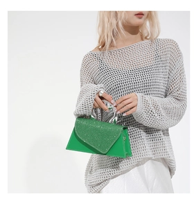 Détail d'un sac trapèze vert à paillettes avec poignée métallique en U sur modèle