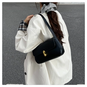 Close-up of a black glossy leather shoulder bag with a vintage gold oval metal buckle