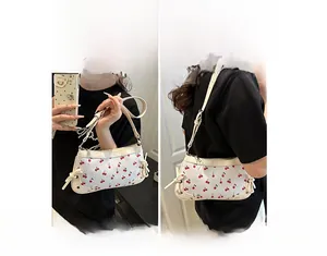 Détail du sac à bandoulière blanc avec imprimé cerise et nœuds décoratifs sur les côtés